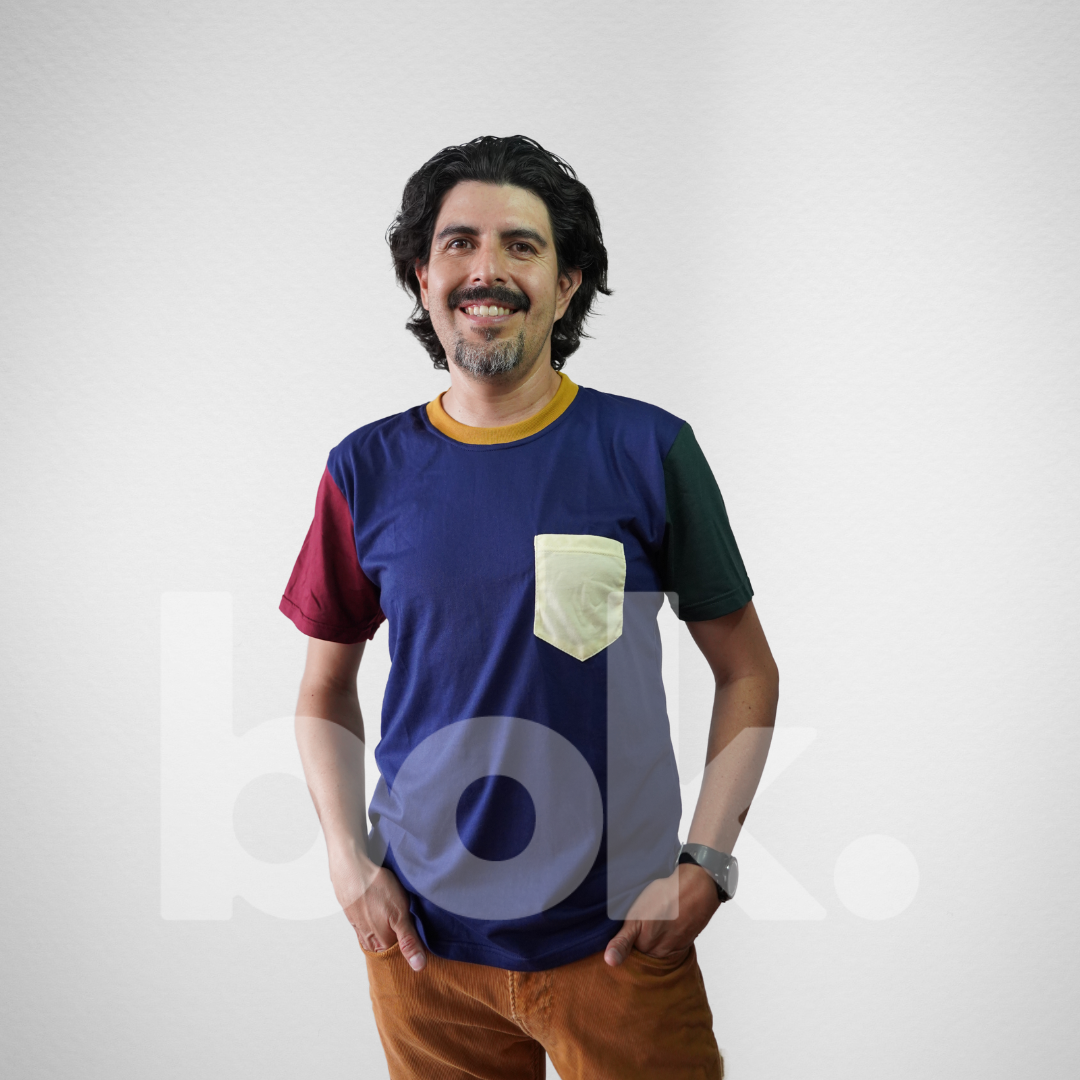 Modelo luciendo una camiseta retro azul con detalles en burdeos, verde y un bolsillo amarillo, combinada con pantalones color mostaza para un look casual y moderno.