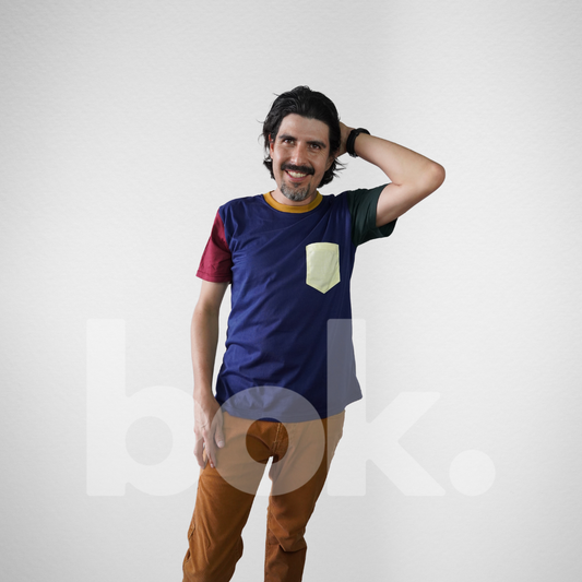 Modelo luciendo una camiseta retro azul con detalles en burdeos, verde y un bolsillo amarillo, combinada con pantalones color mostaza para un look casual y moderno.