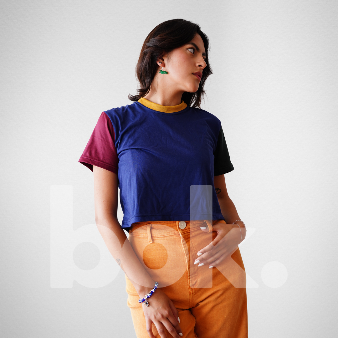 Modelo luciendo un crop top retro azul con detalles en amarillo, verde y burdeos, combinado con pantalones naranja para un look casual y vibrante