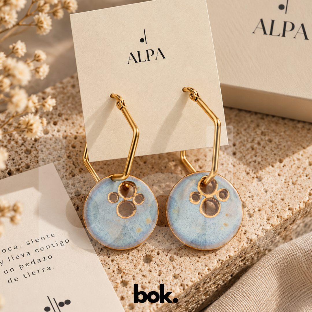 Aretes Luna de cerámica artesanal ALPA hechos a mano en Ecuador, en azul suave con perforaciones inspiradas en cráteres y detalles dorados, disponibles en BOK Concept Store Quito.