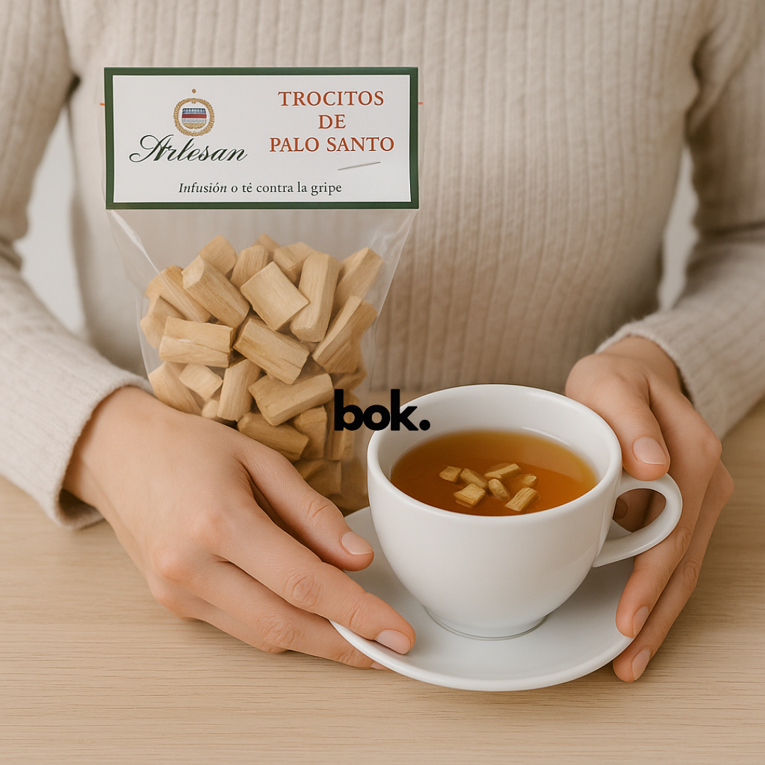 Persona disfrutando una taza de infusión de Palo Santo con trocitos pequeños, junto a bolsa artesanal de BOK Concept Store en mesa de madera clara.