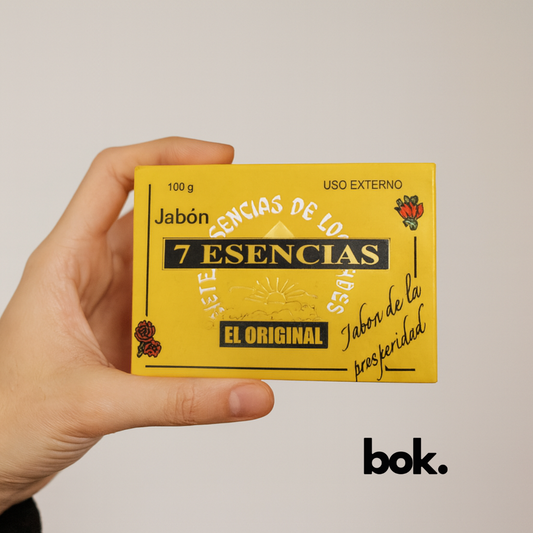 Jabón 7 Esencias artesanal BOK en caja amarilla con diseño clásico, sostenido por una mano sobre fondo neutro, producto natural asociado a la prosperidad.