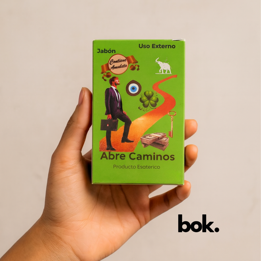 Jabón Abre Caminos artesanal BOK con amuleto, en caja verde con símbolos esotéricos, sostenido por una mano sobre fondo neutro, producto natural para e-commerce.