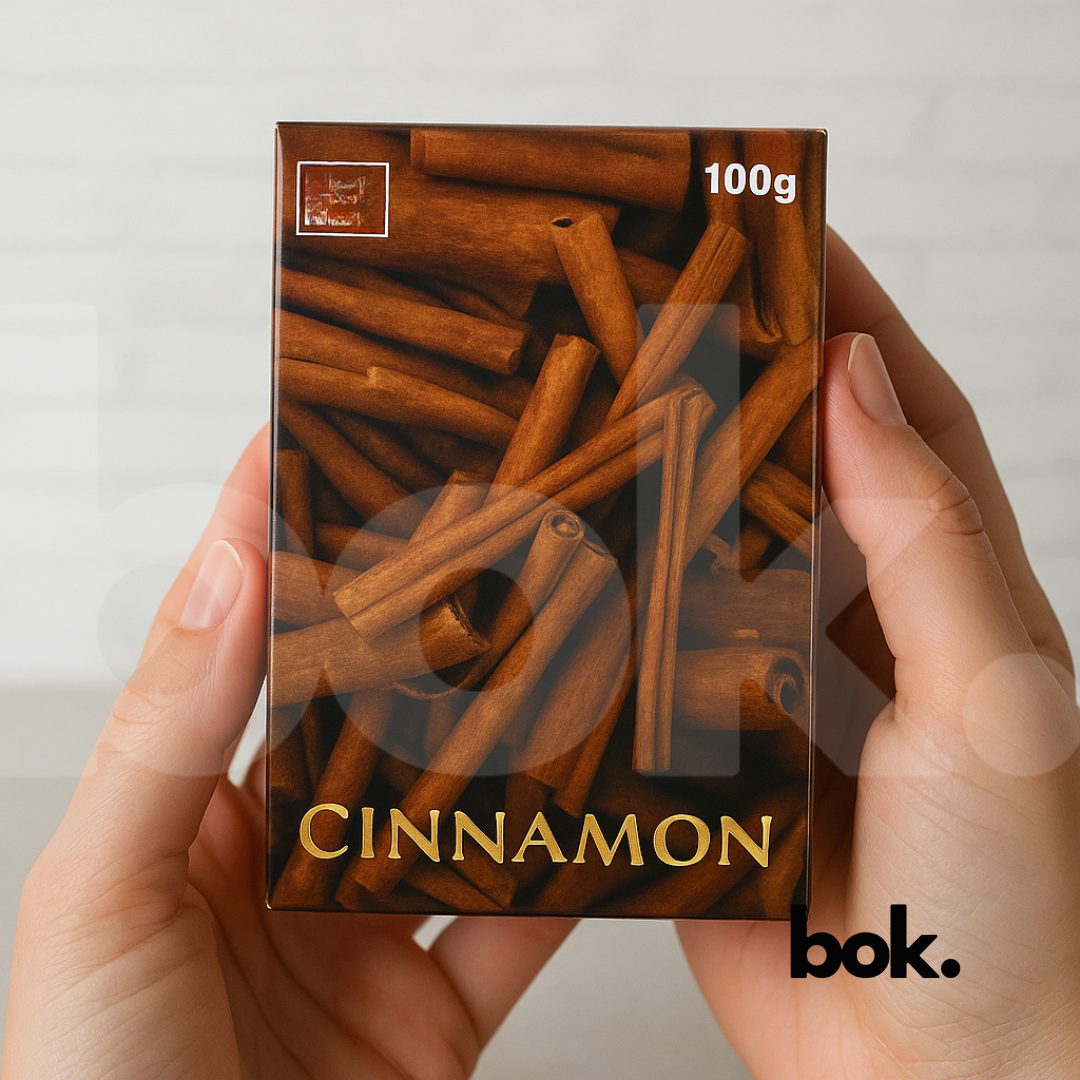 “Jabón de canela natural artesanal de 100 g sostenido entre las manos, con empaque marrón y diseño de ramas de canela — producto de BOK Concept Store ideal para limpieza, equilibrio y bienestar.
