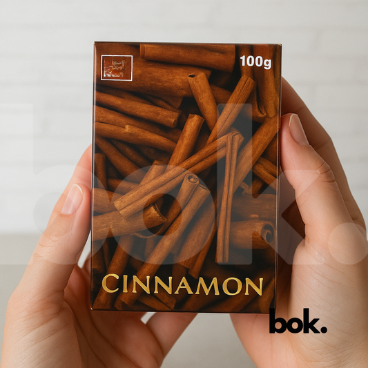 “Jabón de canela natural artesanal de 100 g sostenido entre las manos, con empaque marrón y diseño de ramas de canela — producto de BOK Concept Store ideal para limpieza, equilibrio y bienestar.
