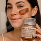 Mujer aplicándose mascarilla exfoliante de barro volcánico de Chachimbiro, sosteniendo frasco de 100 g con etiqueta de Aromas de Cahuasquí - BOK Concept Store