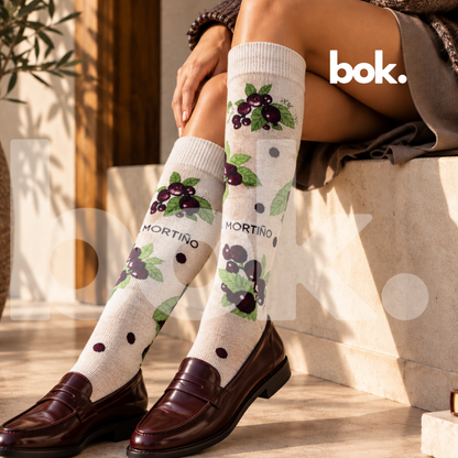 BOK Concept Store Ecuador presenta las Medias Mortiño de Regions by Roland. Modelo luciendo medias largas color crema con ilustraciones de frutos andinos morados y hojas verdes, combinadas con mocasines burdeos de cuero. Accesorios originales de diseño ecuatoriano disponibles en BOK Quito y online.