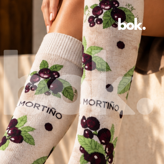 Medias Mortiño disponibles en BOK Concept Store Quito, Ecuador. Primer plano del tejido color crema con racimos de mortiños morados, hojas verdes y pequeños puntos oscuros. Medias largas de diseño ecuatoriano con 75% algodón.