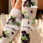 Medias Mortiño disponibles en BOK Concept Store Quito, Ecuador. Primer plano del tejido color crema con racimos de mortiños morados, hojas verdes y pequeños puntos oscuros. Medias largas de diseño ecuatoriano con 75% algodón.