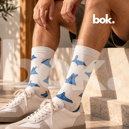 BOK Concept Store Ecuador presenta las Medias Piquero de Patas Azules de Regions by Roland. Hombre luciendo medias largas blancas con diseño azul inspirado en la fauna ecuatoriana, combinadas con shorts oliva y sneakers en un look casual contemporáneo. Accesorios originales disponibles en BOK Quito.