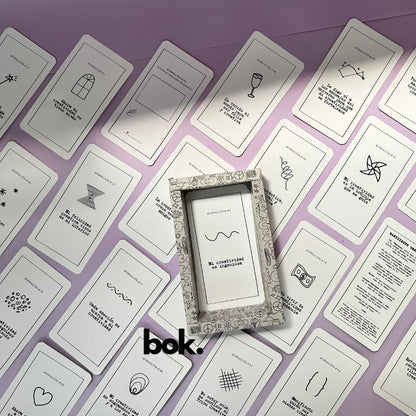 Caja morada del Oráculo Creativo by Vayeca abierta sobre una superficie lila. A su alrededor, varias cartas con frases e ilustraciones minimalistas. El mazo incluye 100 afirmaciones diseñadas para activar y fortalecer la creatividad.