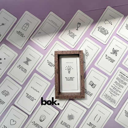 Caja morada del Oráculo Creativo by Vayeca abierta sobre una superficie lila. A su alrededor, varias cartas con frases e ilustraciones minimalistas. El mazo incluye 100 afirmaciones diseñadas para activar y fortalecer la creatividad.