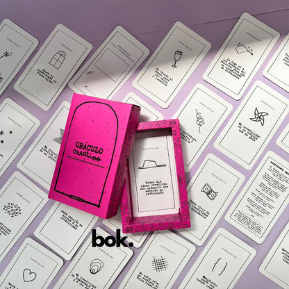 Caja morada del Oráculo Creativo by Vayeca abierta sobre una superficie lila. A su alrededor, varias cartas con frases e ilustraciones minimalistas. El mazo incluye 100 afirmaciones diseñadas para activar y fortalecer la creatividad.