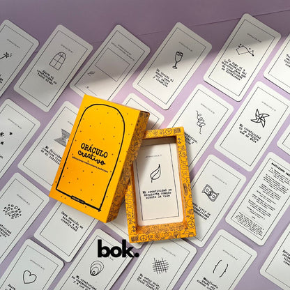 Caja morada del Oráculo Creativo by Vayeca abierta sobre una superficie lila. A su alrededor, varias cartas con frases e ilustraciones minimalistas. El mazo incluye 100 afirmaciones diseñadas para activar y fortalecer la creatividad.