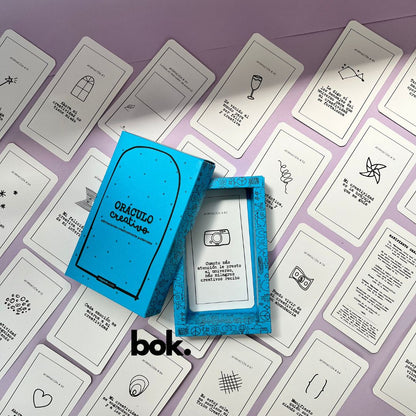Caja morada del Oráculo Creativo by Vayeca abierta sobre una superficie lila. A su alrededor, varias cartas con frases e ilustraciones minimalistas. El mazo incluye 100 afirmaciones diseñadas para activar y fortalecer la creatividad.