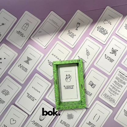 Caja morada del Oráculo Creativo by Vayeca abierta sobre una superficie lila. A su alrededor, varias cartas con frases e ilustraciones minimalistas. El mazo incluye 100 afirmaciones diseñadas para activar y fortalecer la creatividad.