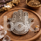 porta inciensos plateado en forma de mano hamsa con ojo protector y grabados artesanales de BOK Concept Store, sobre bandeja de madera en ambiente cálido y elegante con estética espiritual chic